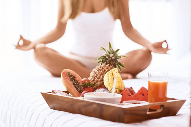 Reach harmony with mind. Close up of tray with fruits in the bed while a young woman practiving yoga in the background