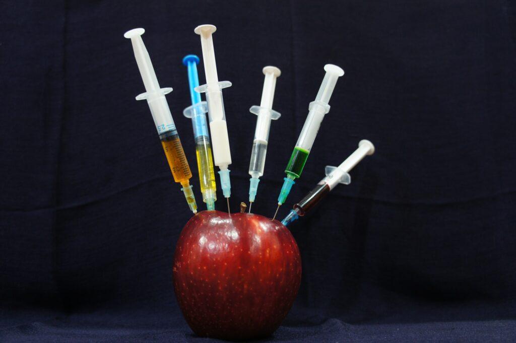 Red apple and plastic syringes on black background