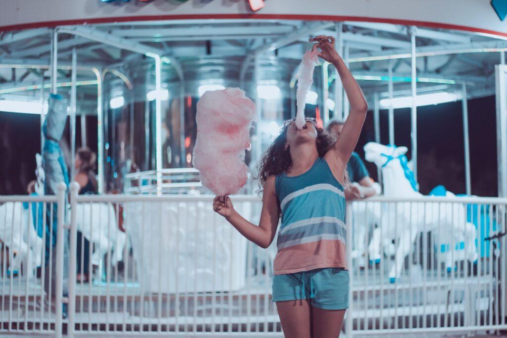 Hungry american woman is eating cotton candy in front of merry-go-round