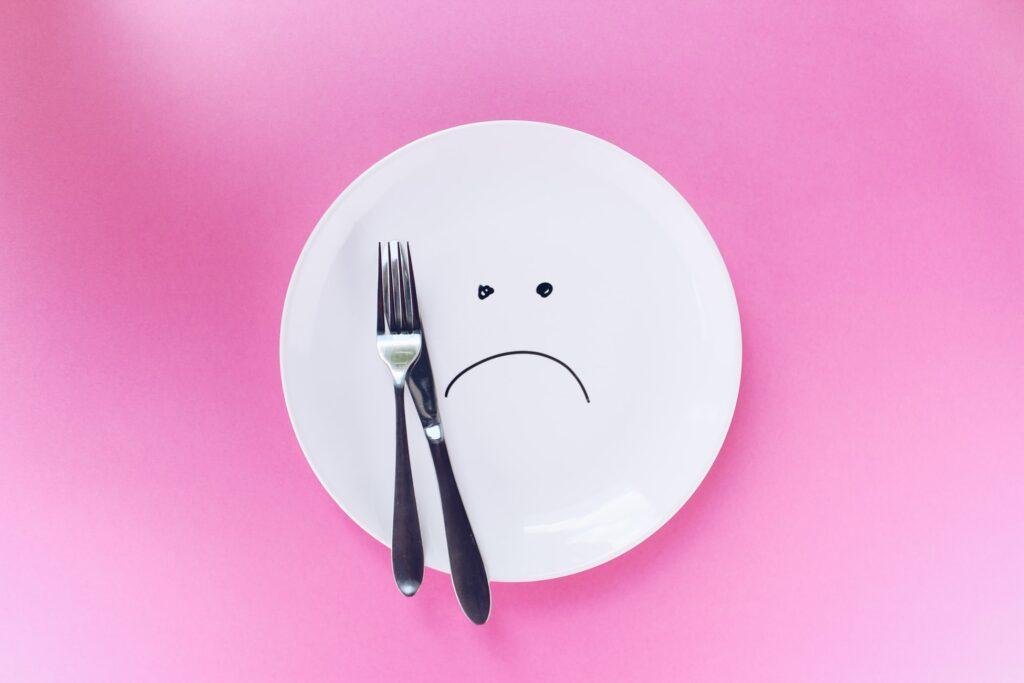 White plate with sad face on the pink background
