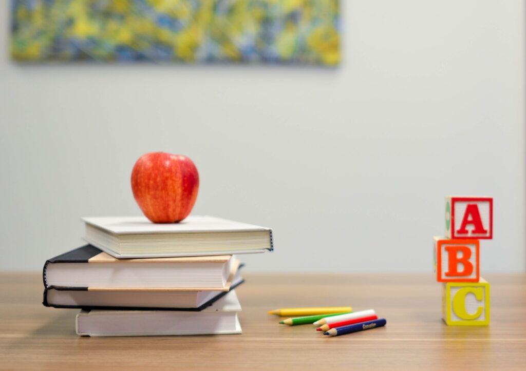 A red apple, books, pencils and letters are on thetable in the classroom