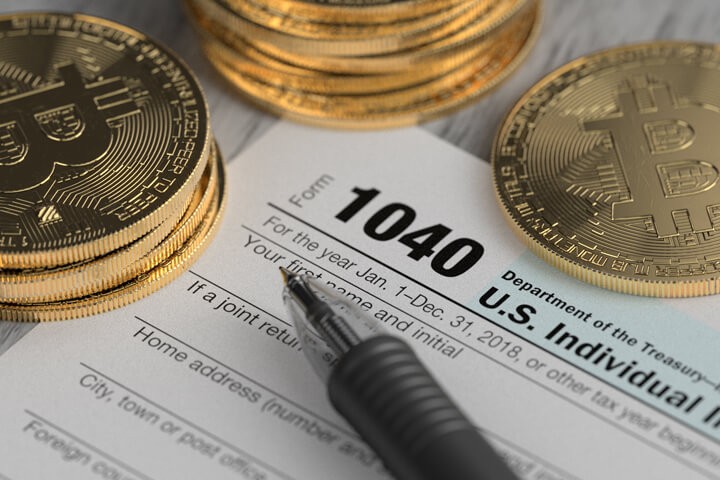 Gold bitcoins placed on a 1040 U.S income tax form with a black pen