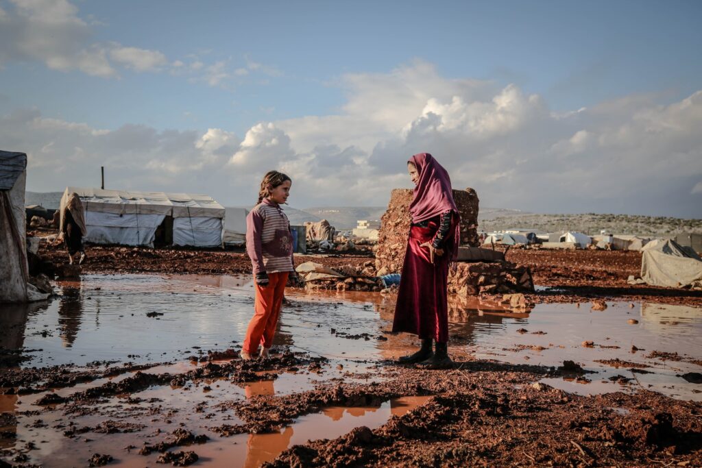 a woman in hijab and a girl standing in a puddle of mud