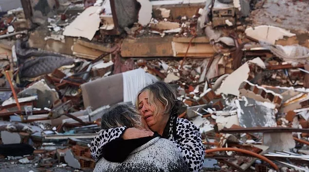 earthquake victims consoling each other in front of a collapsed building